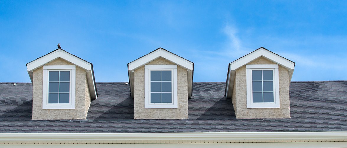 Three square windows jutting out of a rood under a blue sky.